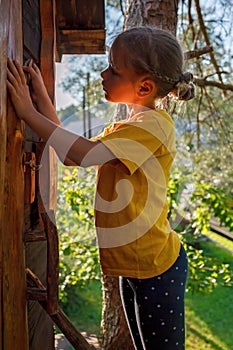 Girl plays in creative handmade treehouse in backyard, summer activity, happy childhood, cottagecore