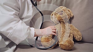 A girl plays a doctor and listens to a toy bear with a phonendoscope.
