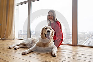 girl plays with a dog breed golden retriever at home on floor, woman with a pet together lies on floor near the window