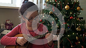 Girl plays dombra against the background of a decorated, Christmas tree