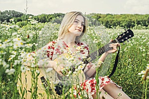 A girl plays the guitar sitting on a flower meadow. Alone with myself.