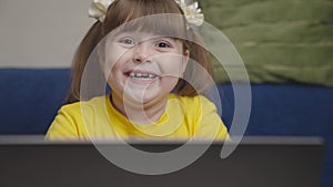 girl plays laptop and waves her hand. face happy kid without tooth close-up. kid does homework laptop. digital computer