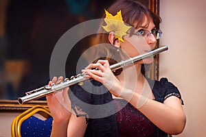 The girl plays a large silver transverse flute. A woman in purple dresses blows a flute at a concert. In the hands of the musician