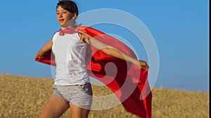 Girl plays superhero running across field with wheat under blue sky