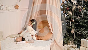 Girl plays with teddy bears, telling them fairy tales and puts them to sleep in her soft four-poster bed. Festive decor with a Chr