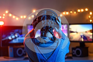 A girl plays video games at a computer. on the background of three monitors. Creative light