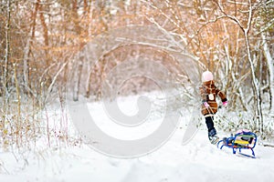 A girl plays in the winter forest at sunset. Children sledding in a snowy park