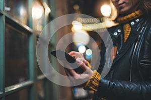 Girl pointing finger on screen smartphone on background bokeh color light in night atmospheric city, hipster using in female hands
