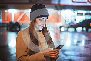 Girl pointing finger on screen smartphone on background illumination bokeh color light in night atmospheric city