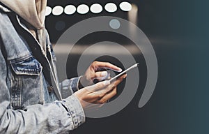 Girl pointing finger on screen smartphone on background illumination bokeh color light in night atmospheric city bridge, hipster