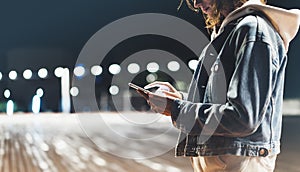 Girl pointing finger on screen smartphone on background illumination bokeh color light in night atmospheric city bridge, hipster