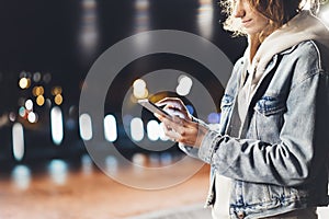 Girl pointing finger on screen smartphone on background illumination bokeh color light in night atmospheric city, hipster using