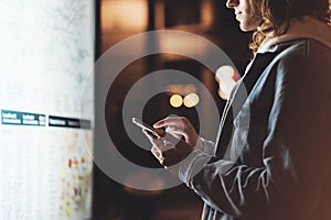 Girl pointing finger on screen smartphone on background light box in night atmospheric city map, hipster using in female hands and