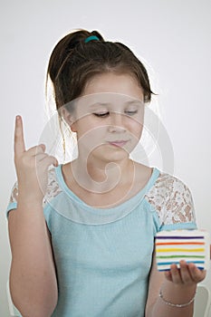 A girl pointing with index figer to the air and with a sguishy toy cake in her hand