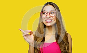 Girl pointing showing on yellow background looking to the side. Very fresh and energetic beautiful young woman smiling happy