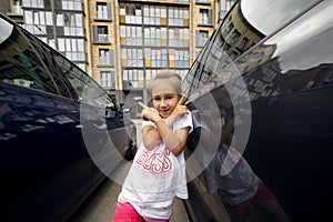 The girl points with her index finger at two different cars standing in an open parking lot in the courtyard of the city.