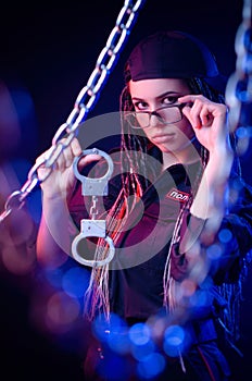 A girl in a police uniform with dreadlocks in neon light with chains and handcuffs English translation the police