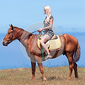 Girl in polka-dot dress rides on brown gelding