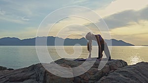 Girl with ponytail does yoga by hills on sea coast at sunrise