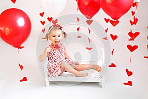 Girl is sitting on a small crib with a large red heart-shaped lollipop