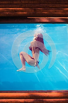 Girl in pool underwater through the glass