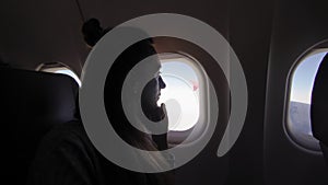 Girl at porthole in the plane. Young woman seating on passenger seat and looking out window on airplane.