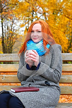 Girl portrait with cup and book on yellow leaves background, autumn season