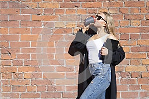 Girl posing against a brick wall. In the hands of a laptop. Drinks cofee