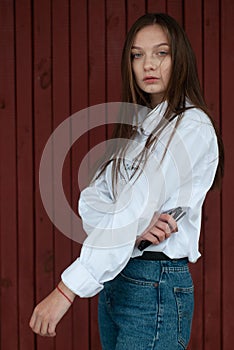 A girl posing against a red background, a young model in a white shirt and with long straight hair
