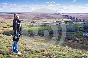 Girl posing on a background of spring rural landscape with drilling rigs in the field