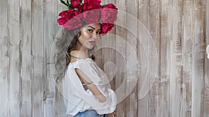 Girl posing in front of camera. young woman in a wreath of scarlet peonies on her head, dark long curly hair descends on