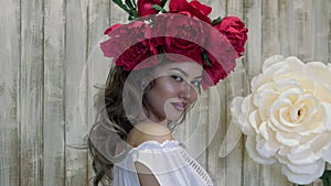 Girl posing in front of camera. young woman in a wreath of scarlet peonies on her head, dark long curly hair descends on