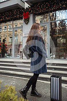 Girl posing on road on winter background. Glamorous funny young woman with smile wearing stylish blue long fur coat