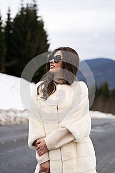 Girl posing on road on winter woods background. Glamorous funny young woman with smile wearing stylish sweater, white