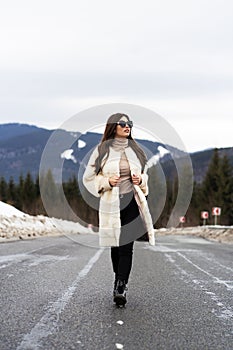 Girl posing on road on winter woods background. Glamorous funny young woman with smile wearing stylish sweater, white