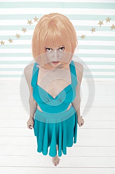 Girl posing striped background of studio. Lady red or ginger wig posing in blue dress. Comic actress concept. Woman