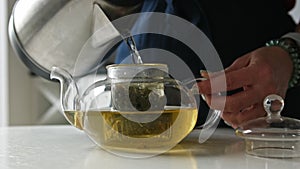 Girl Pouring Hot Water From The Kettle Into Teapot With Green Tea In The Kitchen