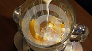 Girl pouring milk in blender with oranges, slow mo