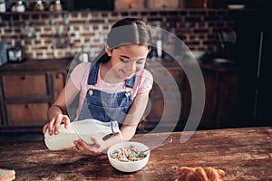 Girl pouring milk into the bowl of corn flakes