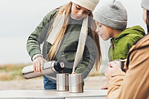 girl pouring tea from thermos for brother