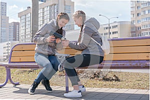 Girl pouring tea from thermos to cup sitting with girlfriend on wooden city bench