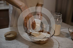 The girl pours the flour into the dough from the glass. The girl prepares the dough for the cake