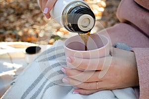 The girl pours hot coffee from a thermos into a cup.