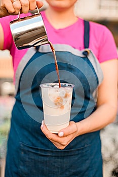 Girl pours hot espresso from a milk pitcher into a glass with an iced drink