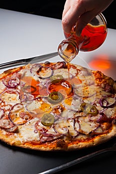 The girl pours a pizza with Bavarian sausages and jalapeno with hot pepper oil