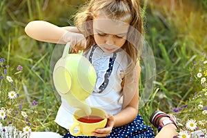 A girl pours tea from a yellow teapot into a cup while sitting in nature in summer. Tea ceremony. Camping.
