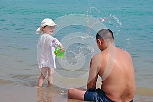 The girl pours water on her father. Splashes of water in the sea. Child and father on vacation.