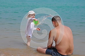 The girl pours water on her father. Splashes of water in the sea. Child and father on vacation.