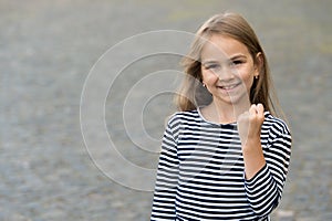 Girl power. Happy girl show fist outdoors. Beauty look of child girl. Little kid smile in stripy top. Casual style