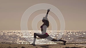 The girl practic yoga on the beach at sunset. Young girl doing exercise at a tropical beach. Silhouette of a woman yoga